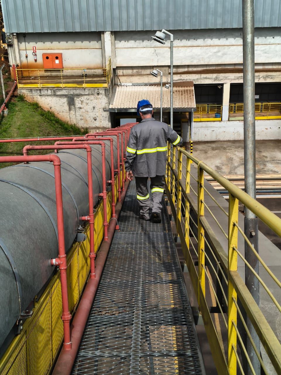 Profissional da IC com uniforme e capacete em passarela industrial elevada